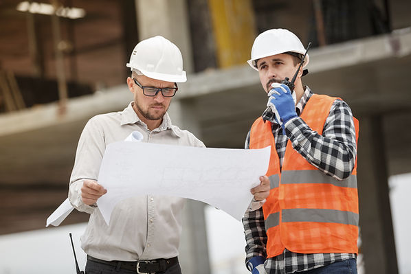 Two men on a construction site. One with a blue print, other on a communication device.